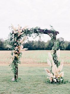 an arch decorated with flowers and greenery in the middle of a grassy field next to a wooden pole