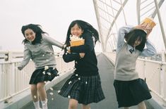 three girls are jumping in the air on a bridge and one girl is holding a book