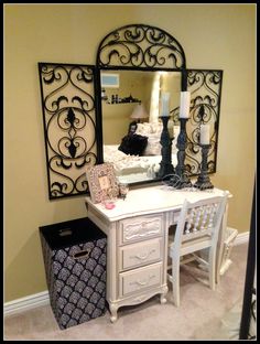 a white desk with a mirror on top of it next to a trash can and lamp