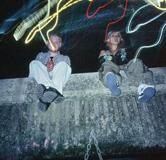 two people are sitting on a ledge with lights in the background