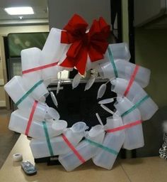 a christmas wreath made out of plastic bottles and ribbon tied around the letters on it