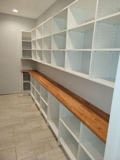 the empty room has white shelving with wooden shelves on each side and tile floor