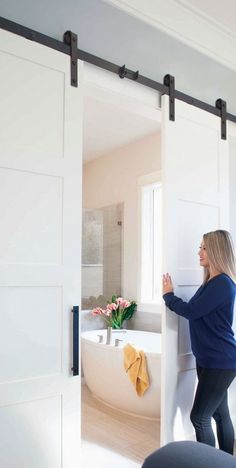 a woman standing in front of a bathroom door holding onto the side of a bathtub