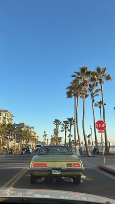 a car is driving down the street near some palm trees and a red stop sign