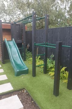 a green slide in the middle of a grassy area next to a black fence and trees