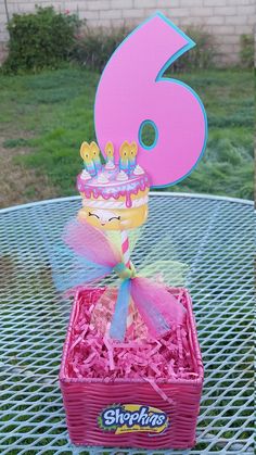 a pink basket with a birthday cake in it on top of a table next to the number six