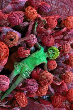 a woman covered in green and orange yarn surrounded by red flowers on a pink background