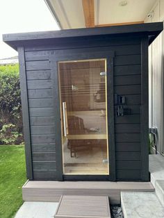 an outdoor sauna with glass doors and bench in the foreground, next to a garden shed