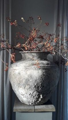 a large vase sitting on top of a wooden table next to a curtained window