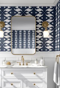 a bathroom with blue and white wallpaper, gold fixtures and a large mirror over the sink