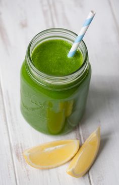 a green smoothie in a mason jar with a blue and white striped straw next to it