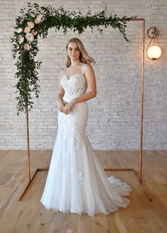 a woman standing in front of a white brick wall wearing a wedding dress with an open back