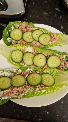 two lettuce leaves with cucumbers on them sitting on a white plate