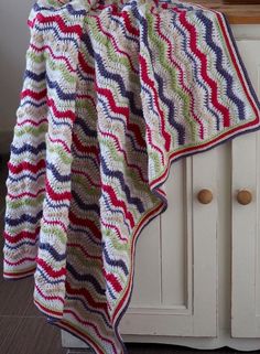 a crocheted blanket sitting on top of a white cabinet next to a window