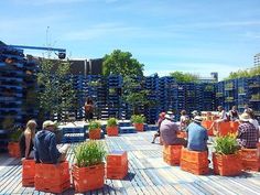 people are sitting on orange crates in the middle of a wooden deck with plants growing out of them