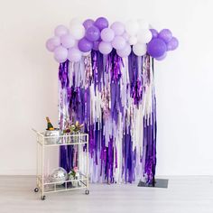 purple and white balloons are hanging on the wall next to a bar cart with drinks