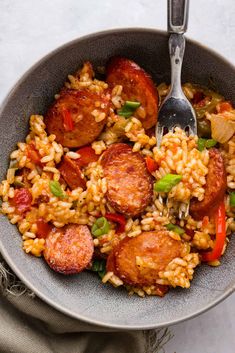 a bowl filled with rice and sausage next to a silver spoon on top of a table