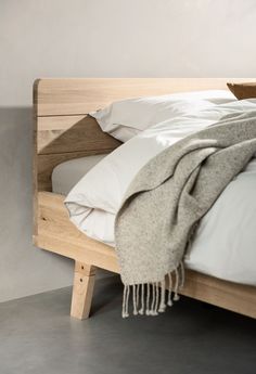 an unmade bed with white sheets and blankets on it's headboard, next to a gray wall