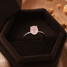 an engagement ring with a pink stone sits in a black box