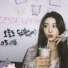 a woman holding a drink in front of a whiteboard with writing on it and an animal figure next to her