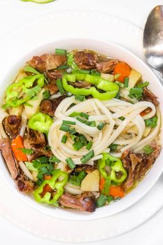 a white bowl filled with noodles, meat and veggies on top of a table