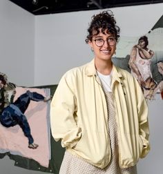 a woman standing in front of some paintings and smiling at the camera with her hands on her hips