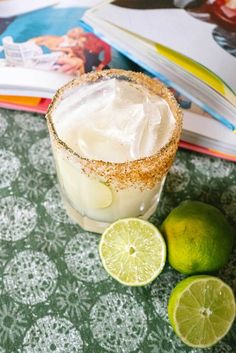 two limes and a margarita on a table next to an open book with the recipe in it