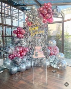 a birthday cake surrounded by balloons and streamers in front of a large window with the words happy birthday written on it