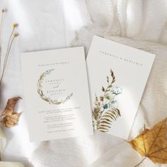 the wedding stationery is laid out on top of white linen with leaves and flowers