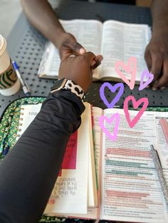 two people sitting at a table with open books and writing on paper in the shape of hearts