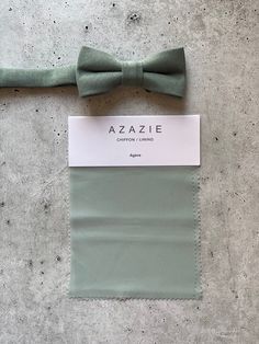 a green bow tie sitting on top of a piece of cloth next to a tag