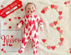 a baby with hearts on it laying next to a sign that says kisses kiss me