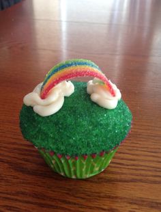 a cupcake with green frosting and a rainbow decoration on top, sitting on a wooden table