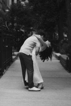 a man and woman kissing on the sidewalk in front of a fenced off area