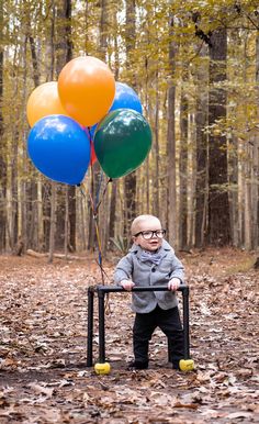 a little boy holding onto some balloons in the woods