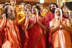 several men in orange and red robes are standing with their hands together while one man is holding a microphone