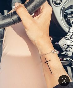 a woman's arm with a cross tattoo on it and a steering wheel behind her