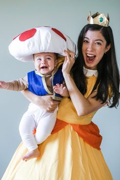 a woman is holding a baby wearing a princess costume while posing for a photo with a mushroom on her head