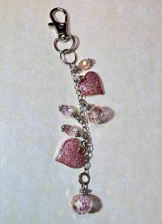 a keychain with charms attached to it on a white surface, featuring hearts and swarovs