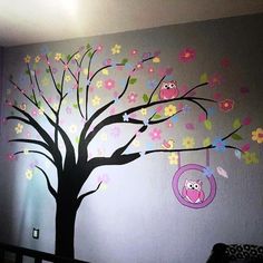 a child's room with a tree painted on the wall and an owl swing