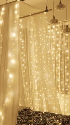 a bed with lights hanging from it's headboard and curtains over the bedspread