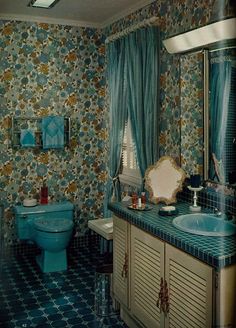 an old fashioned bathroom with blue and gold wallpaper, toilet, sink and mirror