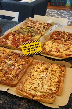 four pizzas in boxes on top of a table with a caution sign next to them