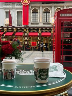 two cups of coffee sitting on top of a table in front of a red phone booth