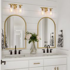 a white bathroom with two sinks and three mirrors on the wall above them are flowers in a vase