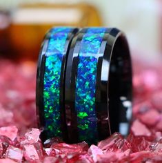 two black rings with blue and green opal inlays on top of pink crystals