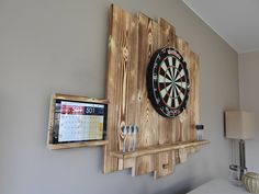 a dart board mounted to the wall next to a calendar on a wooden shelf with darts in it