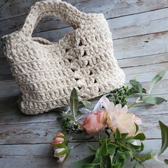 a crocheted bag sitting on top of a wooden floor next to some flowers