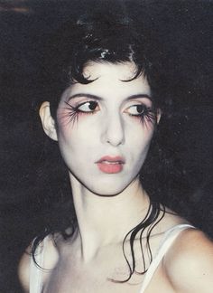 a woman with black hair and makeup has pink eyeliners on her face while wearing a white tank top