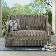 a wicker couch sitting on top of a patio next to a tree and blue rug